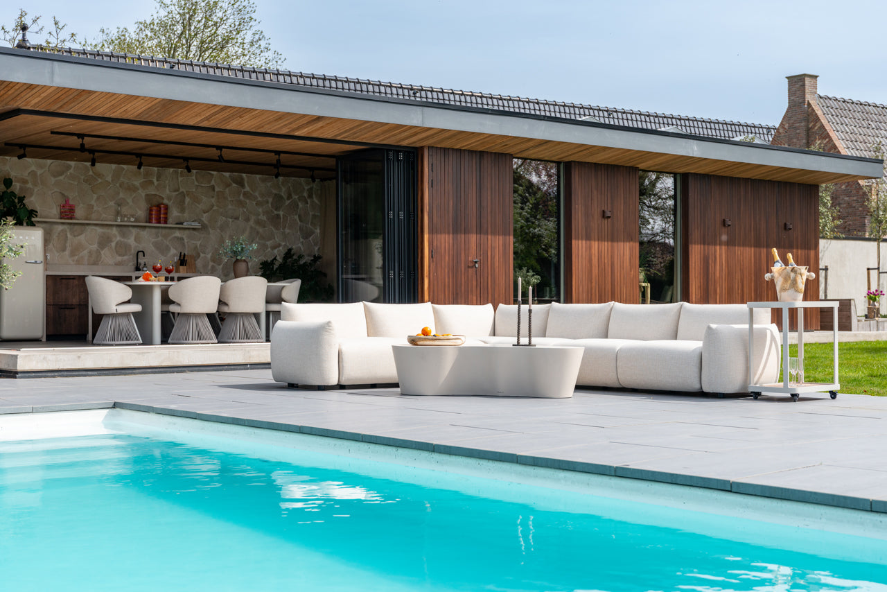 Luxuriöse Outdoor Lounge mit runden Polstermöbeln, Tisch und großer Pflanze im Sonnenlicht