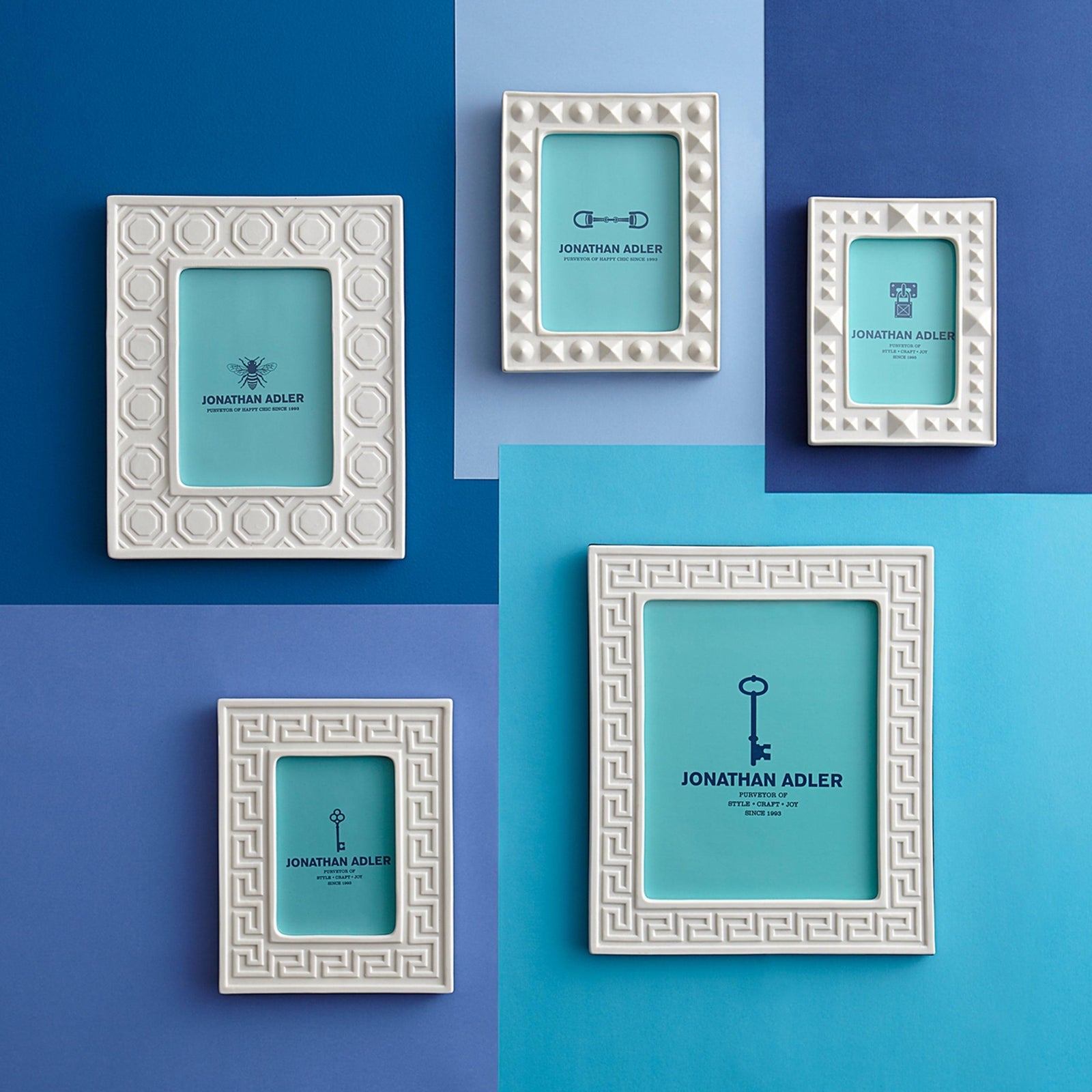 Fünf weiße Jonathan Adler Bilderrahmen mit geometrischem Muster auf blauem Hintergrund, Luxus Deko.