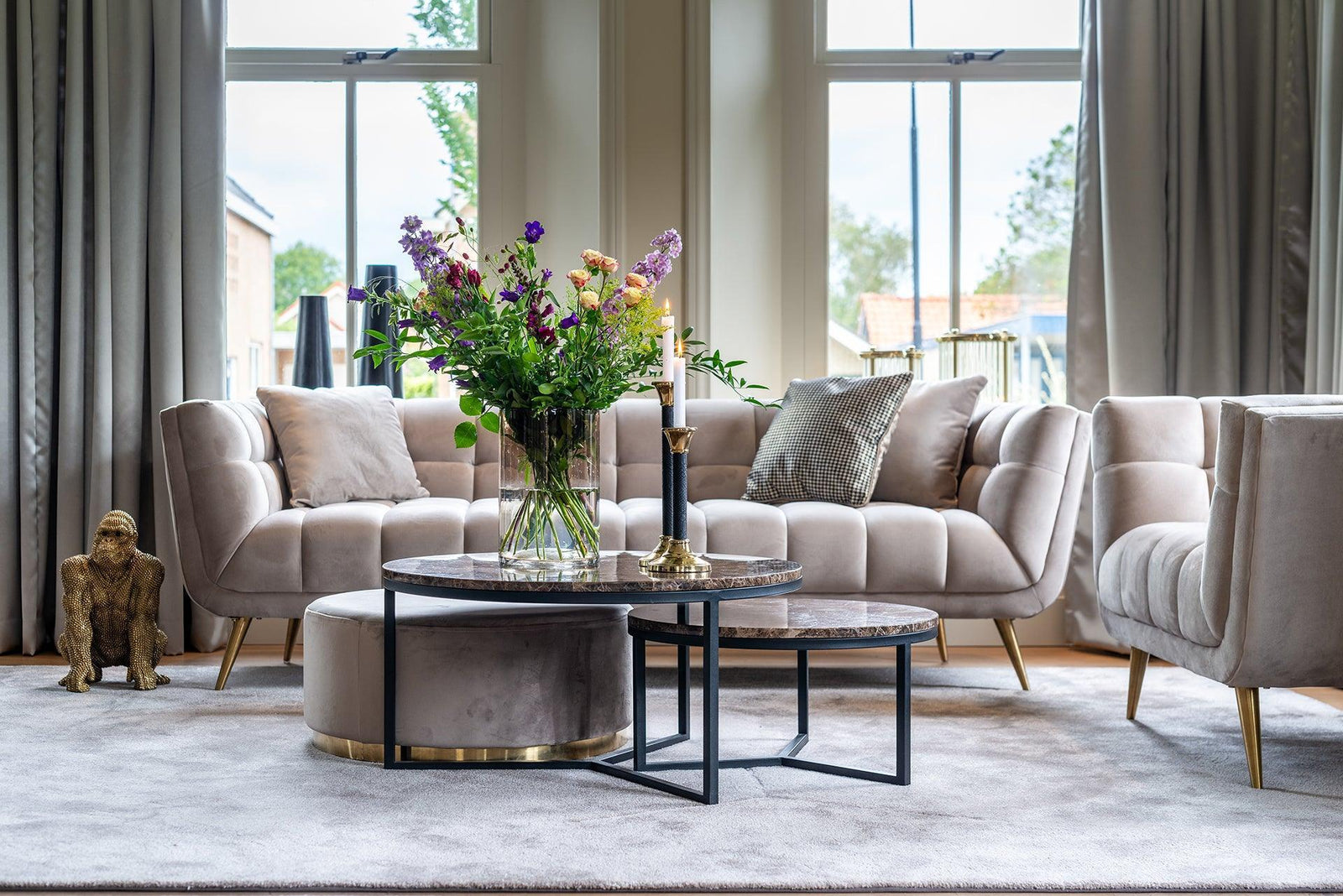 Modernes Wohnzimmer mit beigen Samtsofas, Couchtischen, frischen Blumen und maximalistischem Deko-Style