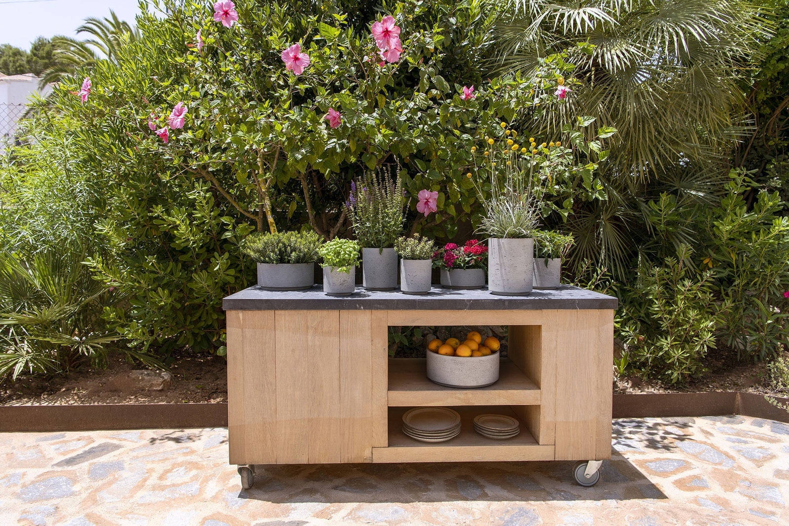 Rough Kollektion Pflanzgefäße aus Beton auf Outdoor-Holztisch vor grünen Pflanzen, Glam Interior