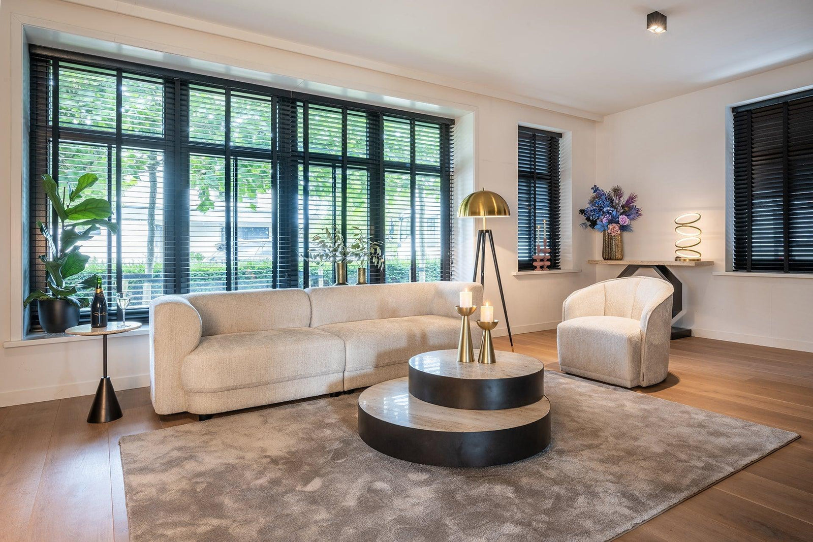 Modernes Wohnzimmer mit Creme-Sofa, Design-Sessel, runder Couchtisch, goldener Stehlampe und großen Fenstern, Richmond Interiors Avalon Kollektion bei Codeso Living