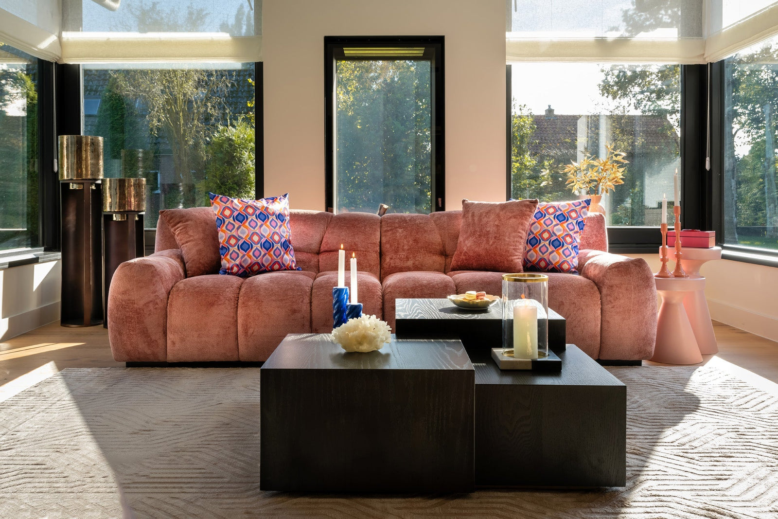 Modernes Wohnzimmer mit rosa Samtsofa, bunten Kissen, Kerzenständern und stilvollen Teelichthaltern von Codeso Living