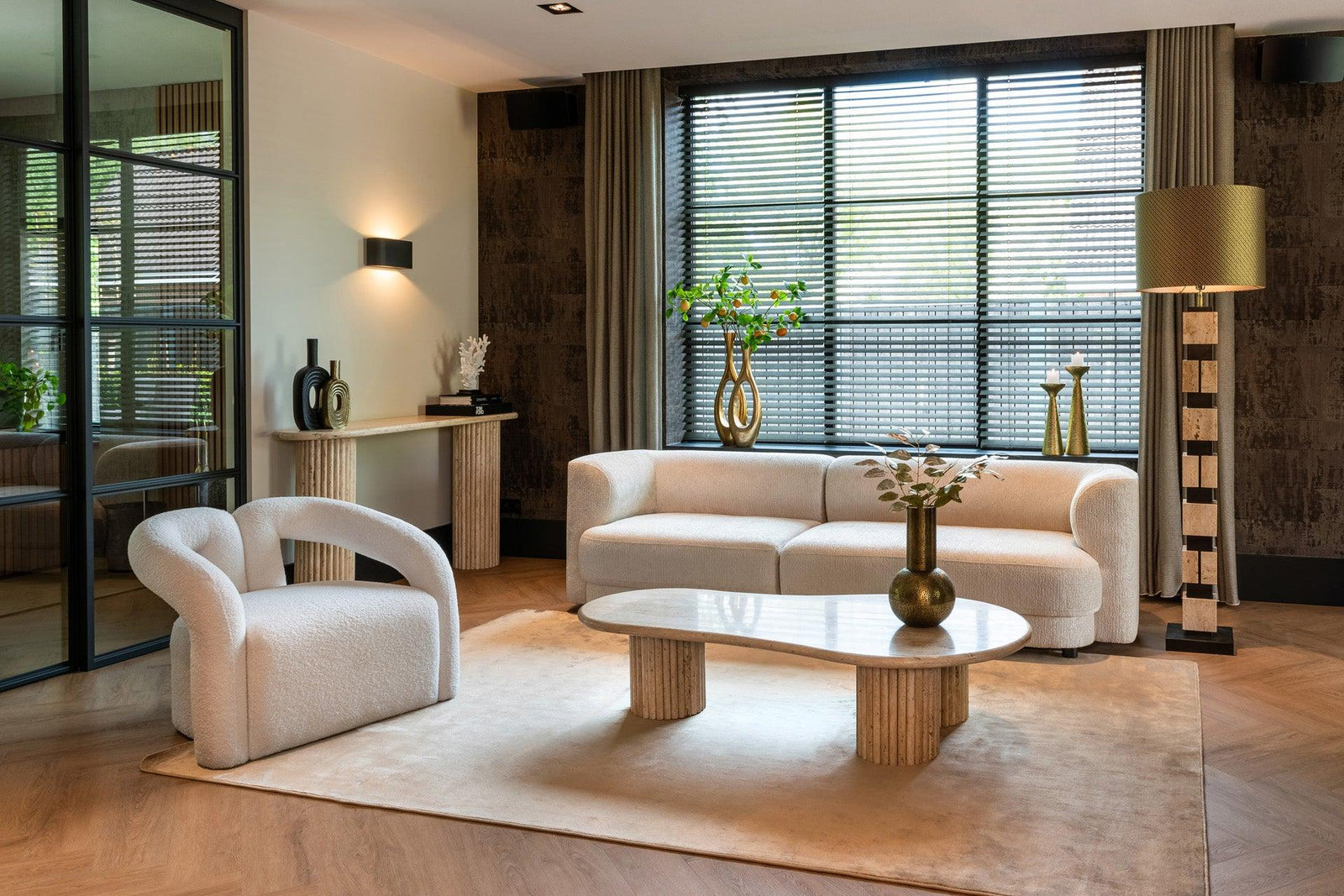 Modernes Wohnzimmer mit cremefarbenem Sofa, Design-Sessel, Travertin-Konsolentisch und goldenen Deko-Elementen im luxuriösen Maximalismus-Stil von Codeso Living.